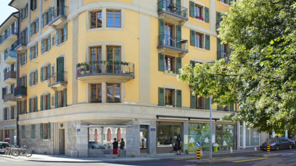 A yellow multi-story building with balconies and green shutters.