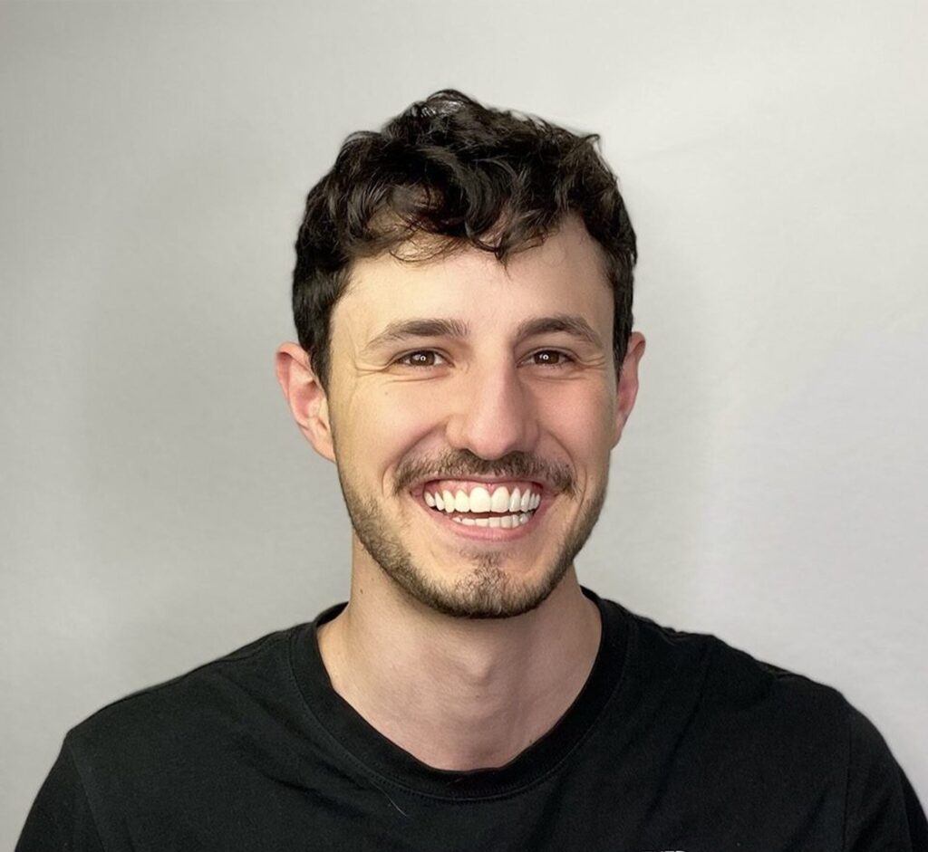 Smiling man with dark curly hair and beard in black t-shirt.