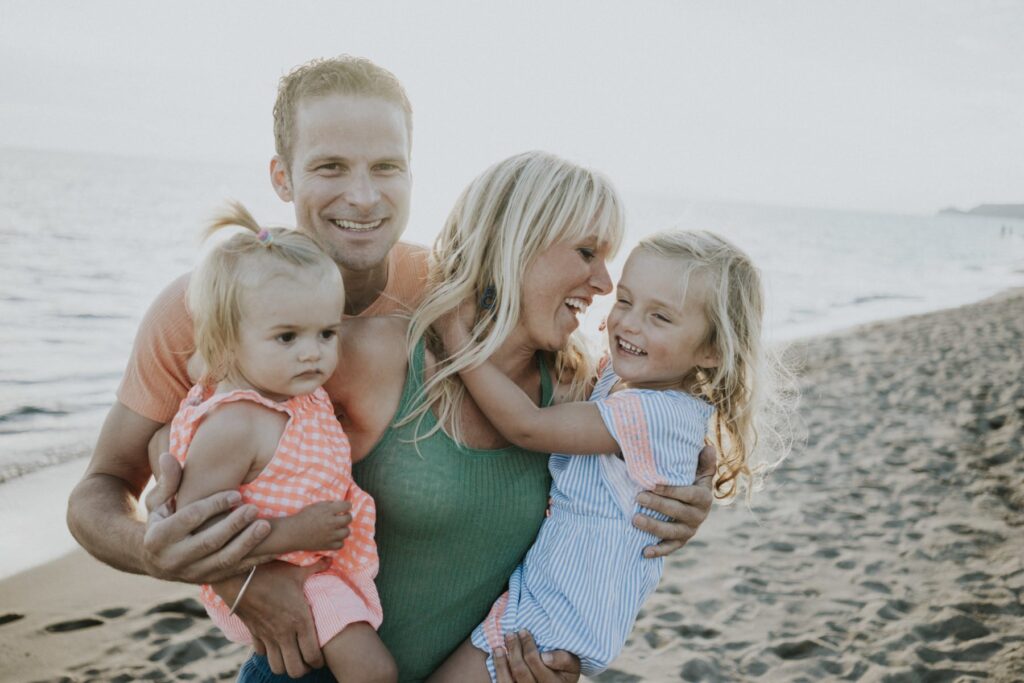 A family of four on the beach, with two adults and two young girls.