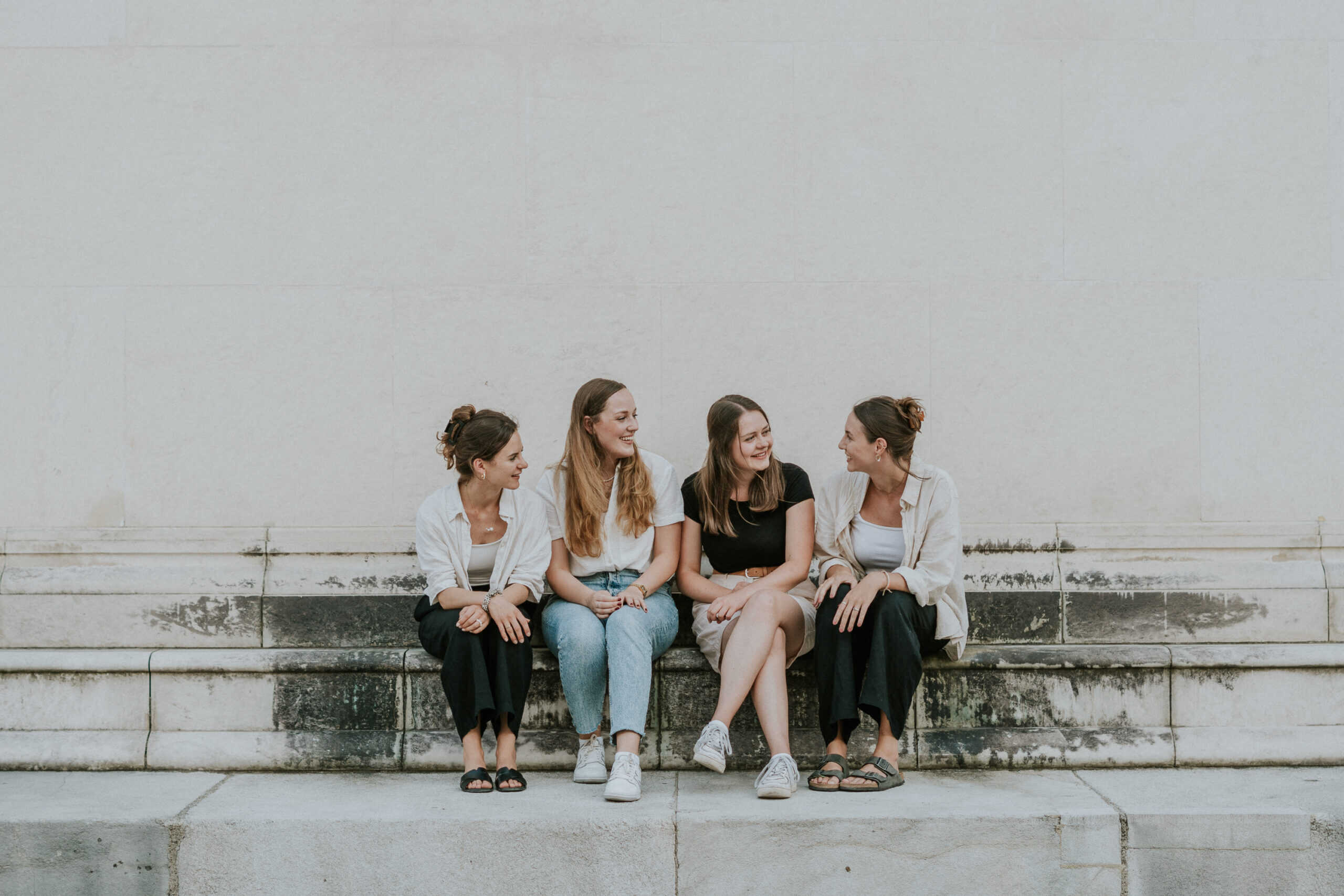 Lebendige Frauen, die gemeinsam draußen auf einer Steinbank sitzen, lachen und sich unterhalten, symbolisieren Gemeinschaft und Freundschaft in einer modernen Kirche.