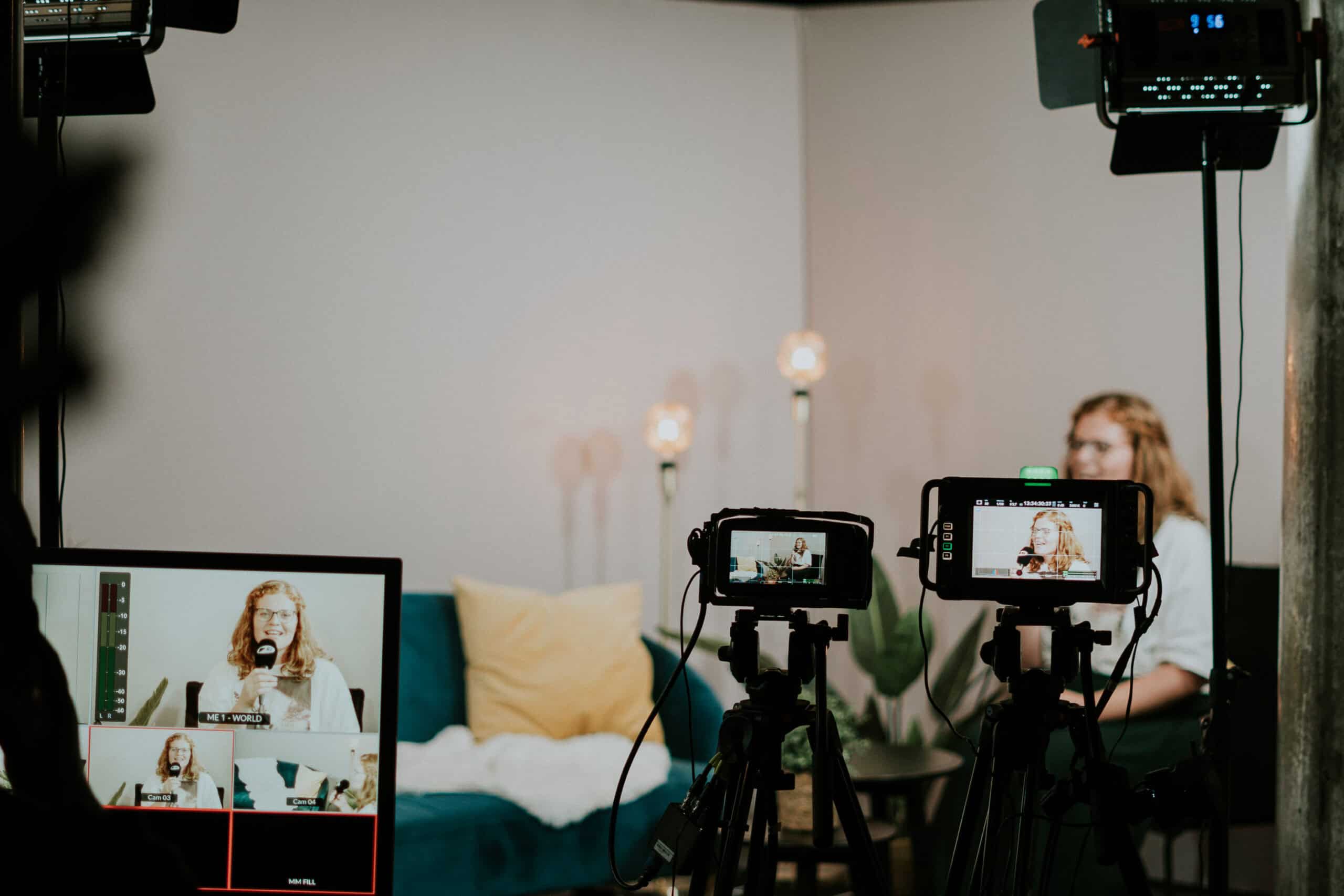 Ehefrau im Videochat während einer Live-Übertragung, auf einer Couch mit Kissen, in Hintergrund Pflanzen und Stehlampen, Kamera- und Lichttechnik im Einsatz, professionelle Aufnahme für Online-Gottesdienst oder Event.