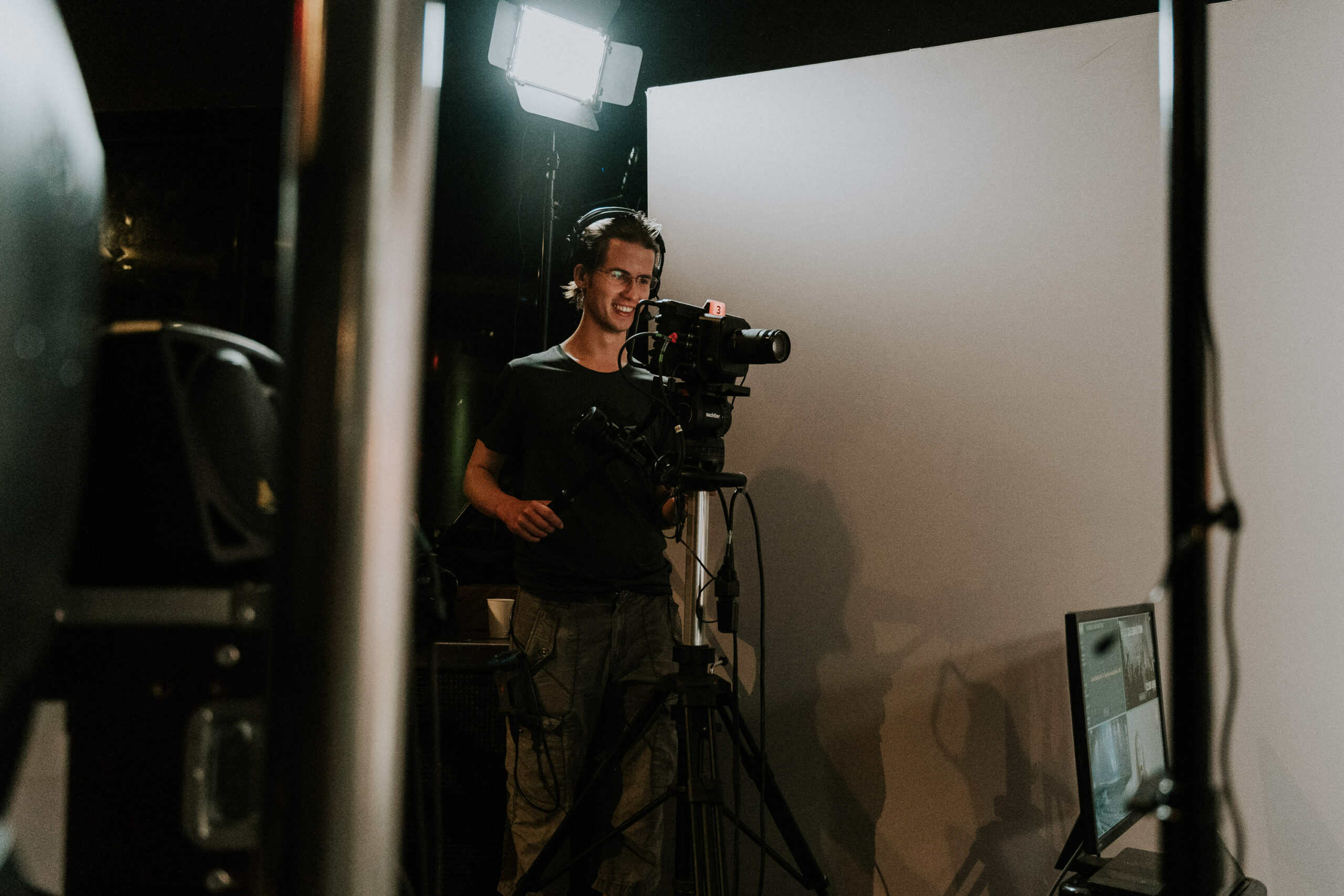 Aufnahme eines jungen Mannes vor einer Kamera bei der Video-Produktion in einem dunklen Studio. Professionelle Videotechnik und Lichtsetup, ideal für Online-Gottesdienste, Predigten oder christliche Events.