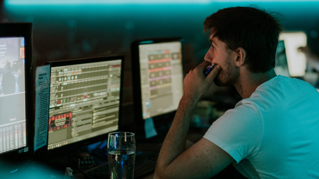 Mann arbeitet an mehreren Computern mit Musiksoftware in einem dunklen Raum.
