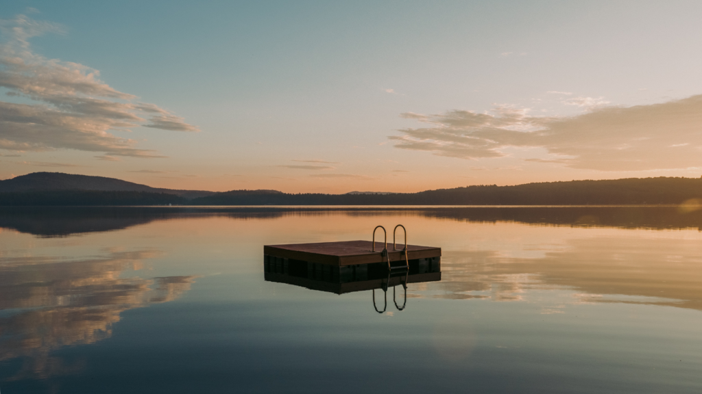 Schwimmsteg im ruhigen See bei Sonnenuntergang, Himmel mit Wolken.