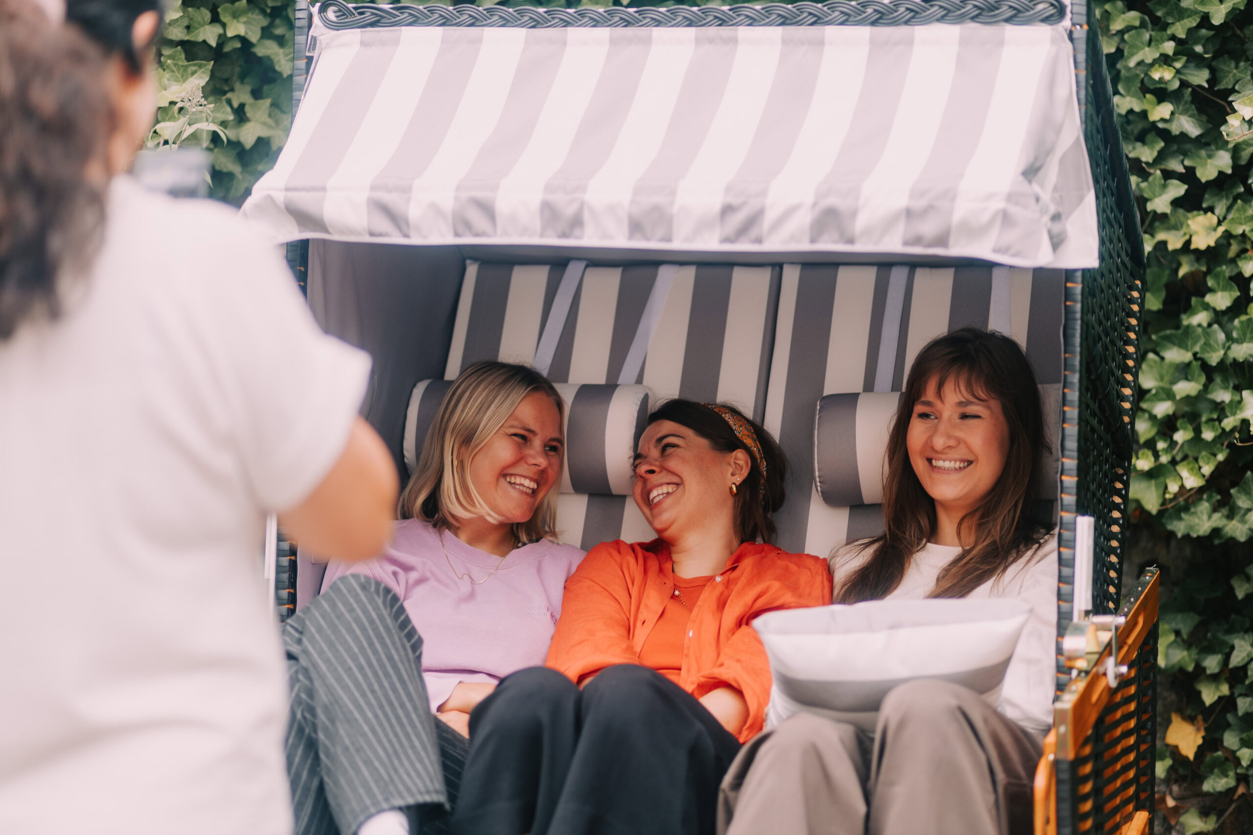 Entspannte Frauen lachen zusammen in einem Strandkorb, ideal für entspannte Tage im Freien und Gemeinschaft am Wasser, perfekt für Familien- oder Freundesausflüge.