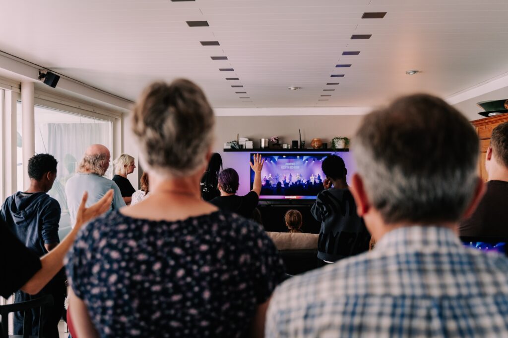 Menschen beim Gottesdienst in Hamburg, die gemeinsam auf eine große Leinwand schauen, in einem modernen Kirchenraum mit natürlichem Licht.