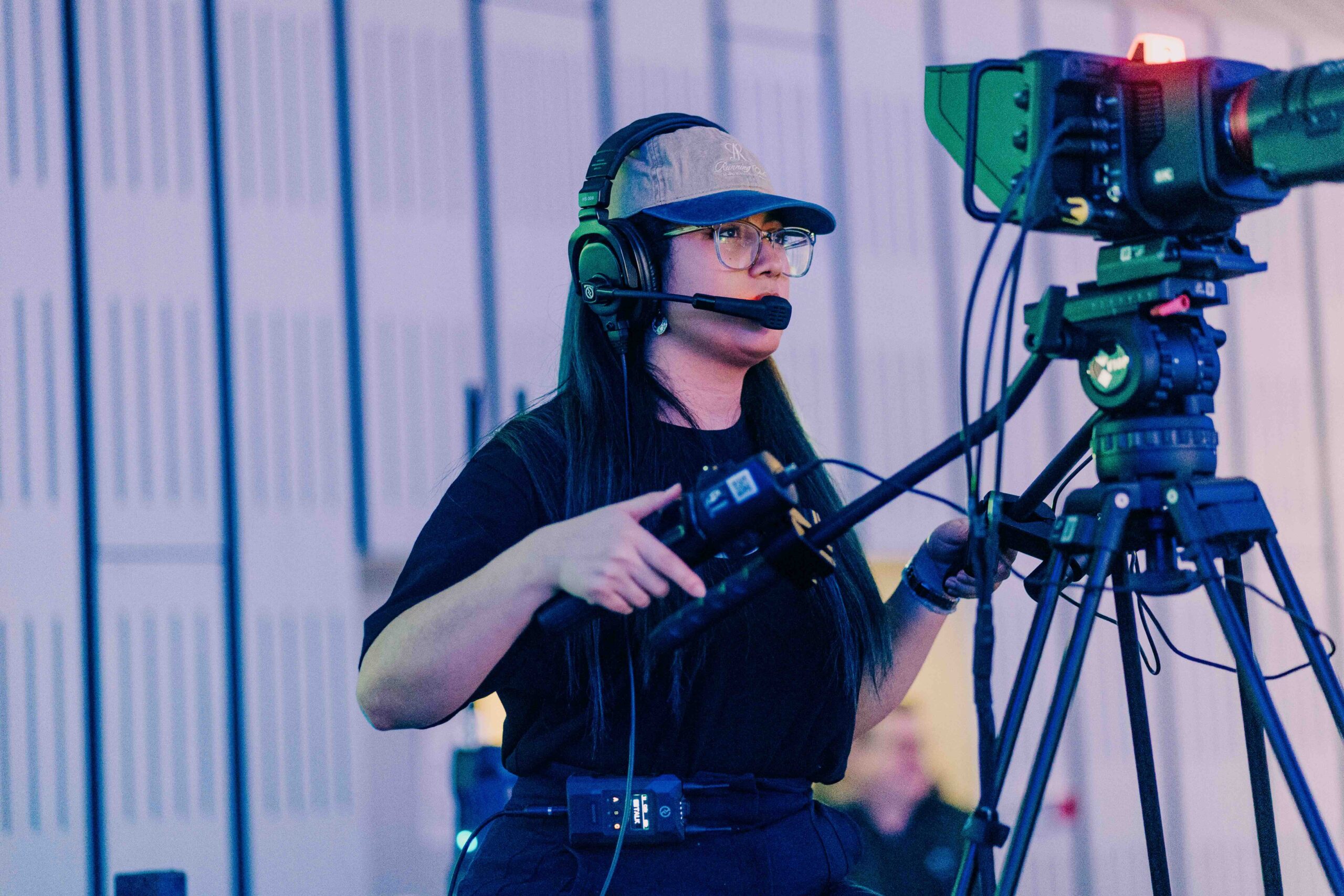 Frau mit Headset und Kamera bei der Produktion eines Films oder Events, professionelles Filmen in einem Studio oder Veranstaltungsraum.