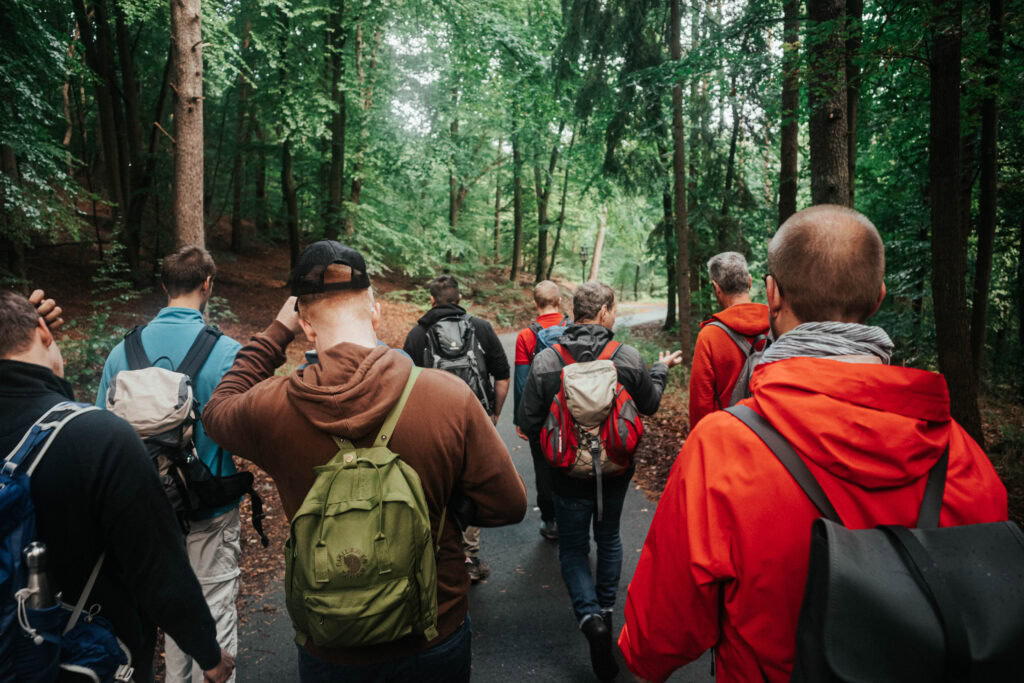 Gruppe von Menschen mit Rucksäcken wandert durch einen Waldweg.