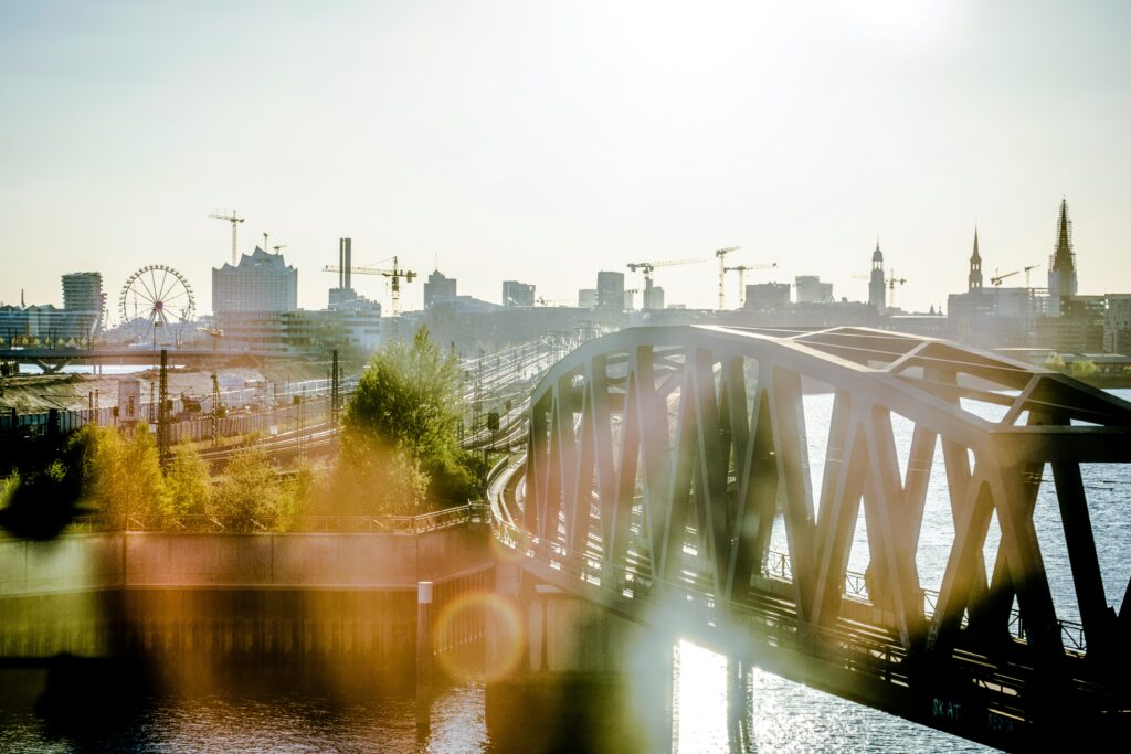 Ein Blick auf eine Brücke über Wasser mit Stadt im Hintergrund, Baukräne und Türme sichtbar.