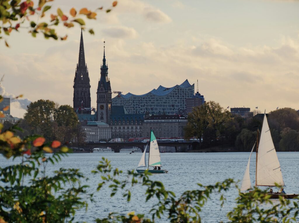 Zwei Segelboote auf der Elbe mit Hamburgs Skyline und Kirchen im Hintergrund.