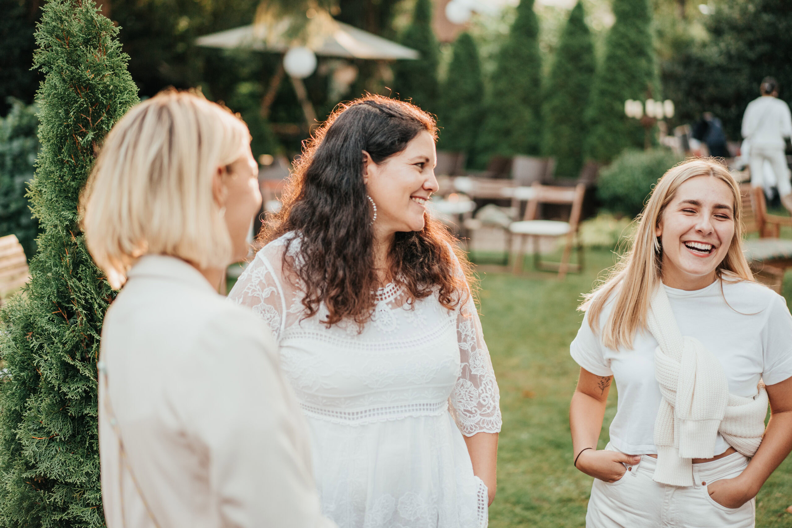 Drei Frauen stehen im Garten, lachen und unterhalten sich.