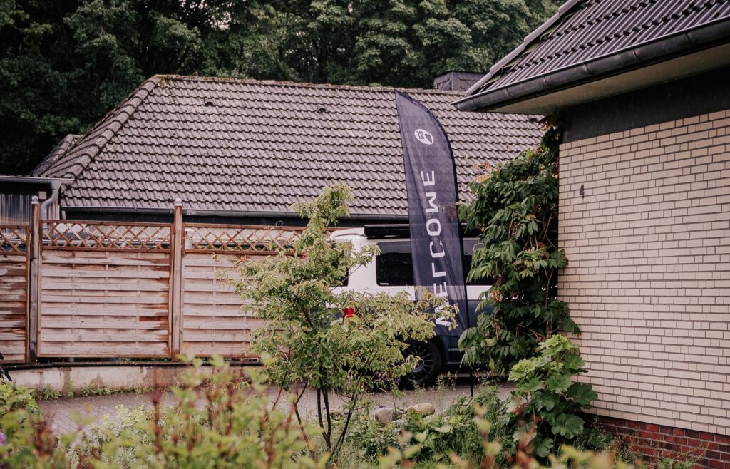 Flagge mit "Micro Church" Text vor einem Haus, umgeben von Büschen und Bäumen.