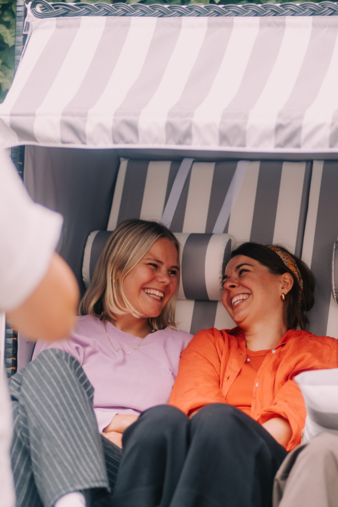 Zwei lachende Frauen sitzen im Zelt, unterhalten sich.