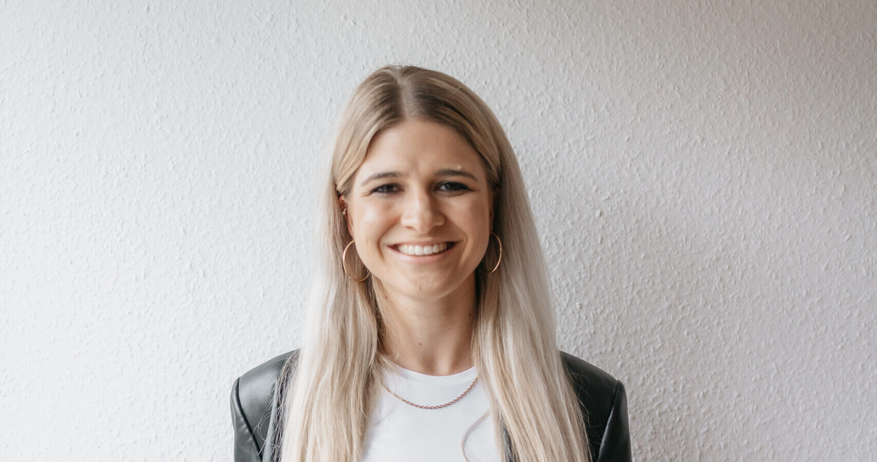 Ein junges, freundliches Mädchen in schwarzem Lederjacke und weißen T-Shirt steht vor weißer Wand, lächelt natürlich, wirkt offen und einladend. Perfekt für Glaubens- und Gemeinschaftsangebote bei ICF Heilbronn.