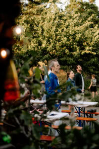 Gruppe von Menschen steht im Freien bei einem Weihnachtsmarkt, Bäume im Hintergrund.