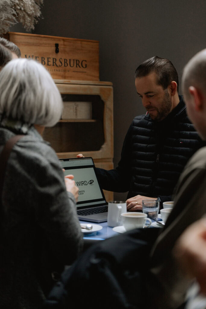 Vier Personen sitzen um einen Tisch, schauen auf einen Laptop.