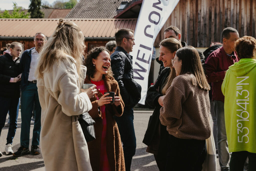 Fröhliche Menschen beim Gemeinschaftstreffen im Freien, lachend und im Gespräch, mit ICF Banner im Hintergrund, bei einem evangelischen Gottesdienst oder Gemeinschaftsveranstaltung.