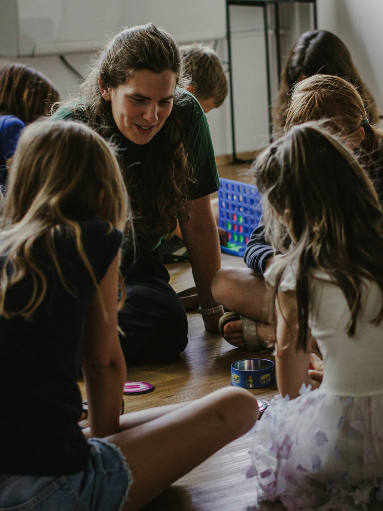 Menschen spielen gemeinsam Spiele auf dem Boden, eine junge Frau leitet und begleitet Kinder bei einer Freizeitaktivität. Ideal für Familien, Kinder und Jugendliche, christliche Gemeinschaft, gemeinsame Spiele, Spaß und Gemeinschaft bei ICF Herrenberg.