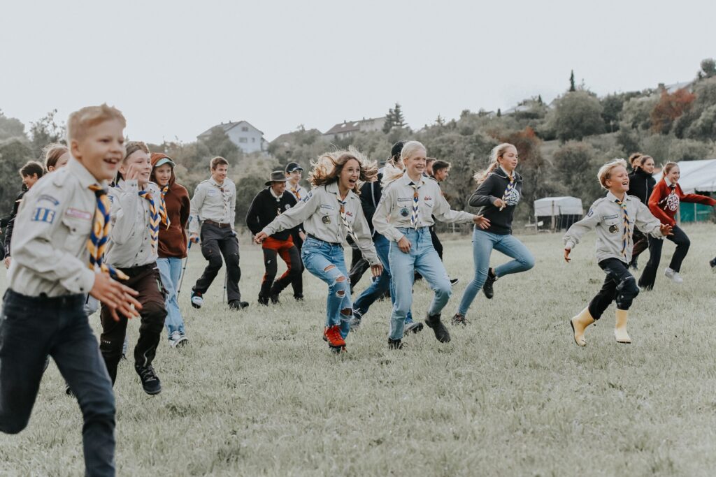 Kinder und Jugendliche beim fröhlichen Spielen auf einer grünen Wiese, in Pfadfinderuniform mit Scouts-Abzeichen und Halstuch, bei einem Outdoor-Event in Herrenberg.