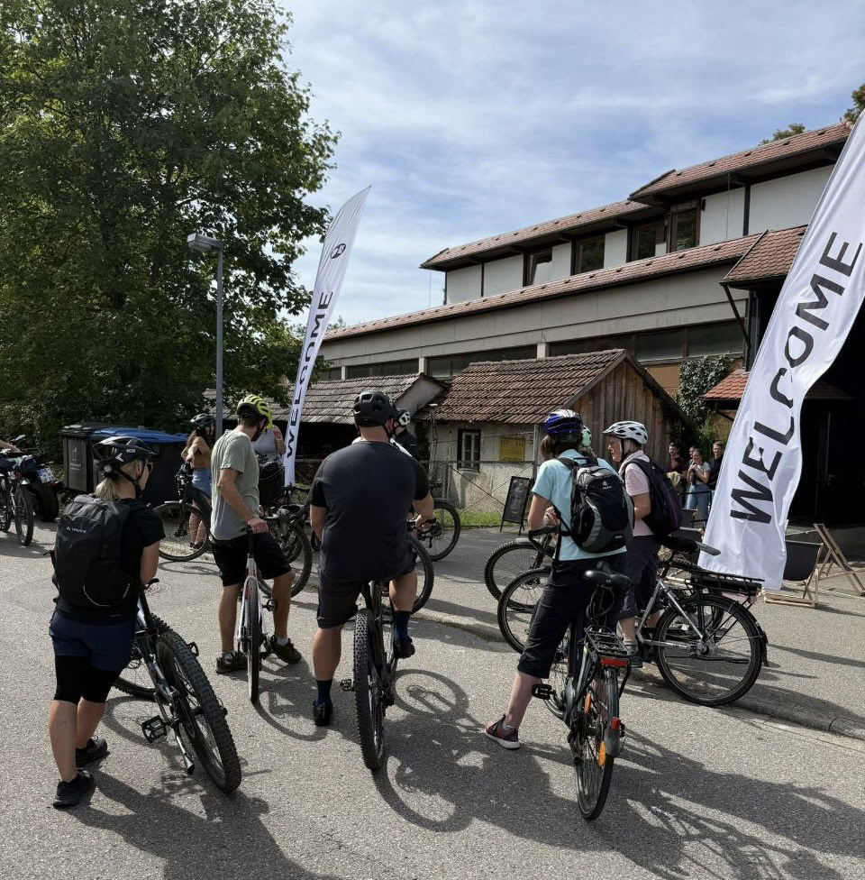 Fahrradgruppe vor dem Gemeindehaus in Herrenberg, die auf den Start einer Fahrradtour wartet, mit Willkommensflaggen und entspannten Teilnehmern.