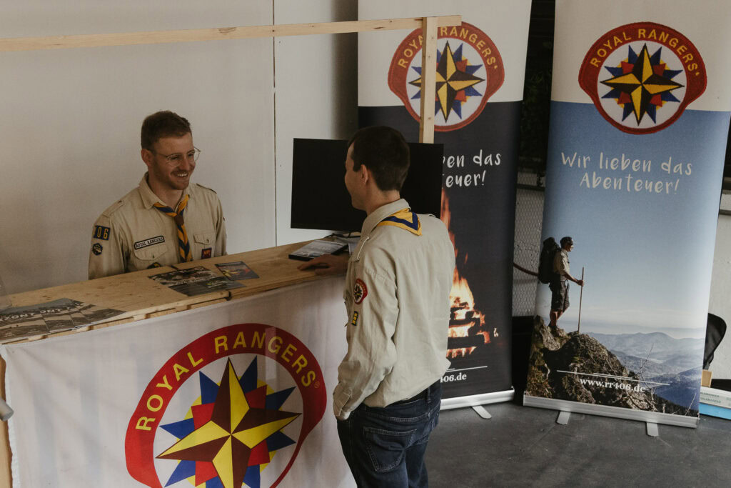 Zwei junge Männer in Scout-Uniformen sprechen an einem Stand mit Royal Rangers Bannern.