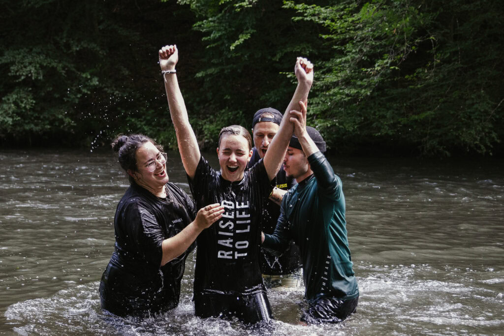 Vier Menschen stehen im Fluss, eine Person hebt die Arme in Siegerpose.