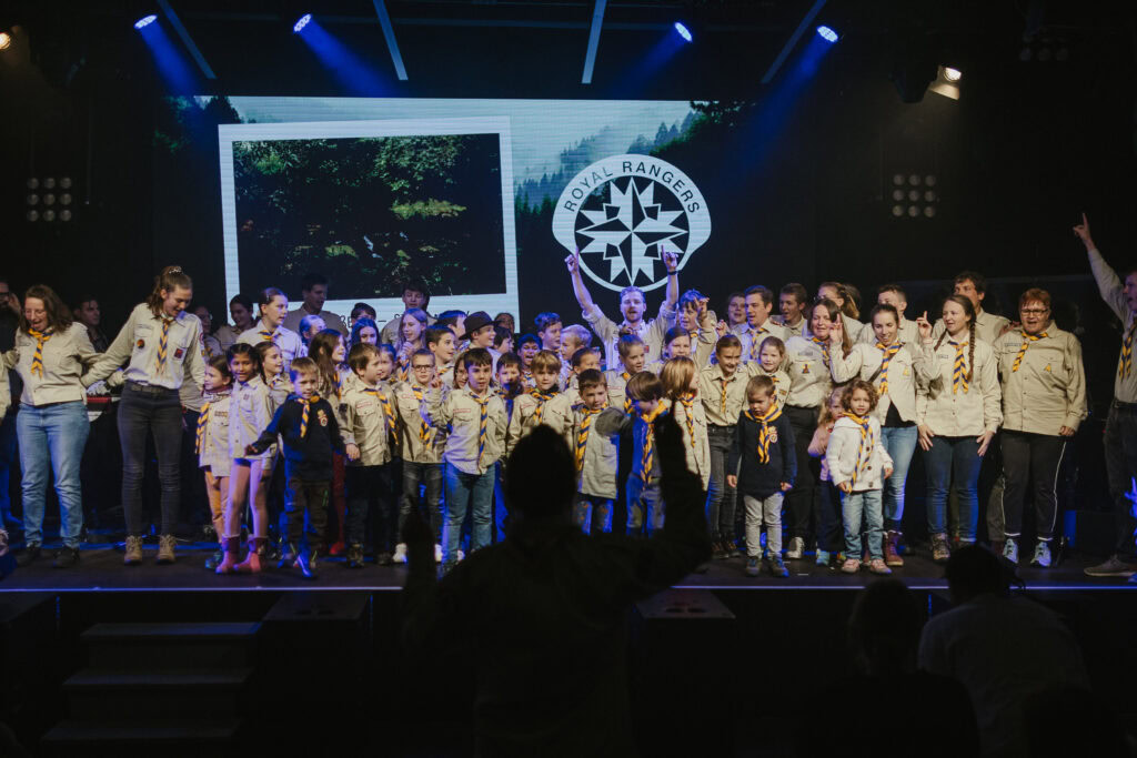 Gruppenfoto von Kindern und Jugendlichen auf einer Bühne, einige tragen Uniformen mit Halstüchern.