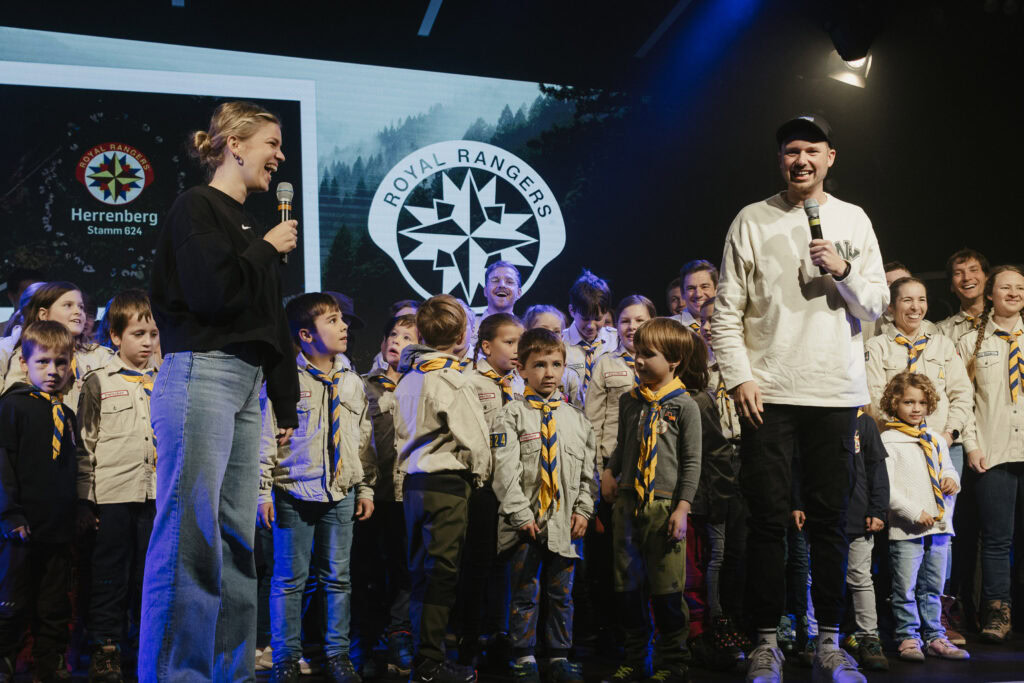 Kinder und Erwachsene auf Bühne bei Royal Rangers Herrenberg, zwei Personen sprechen.