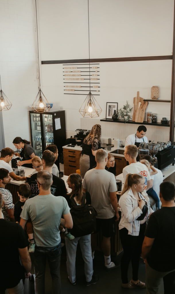 Menschen stehen in einer Kaffeebar-Schlange, einige bestellen, andere warten.