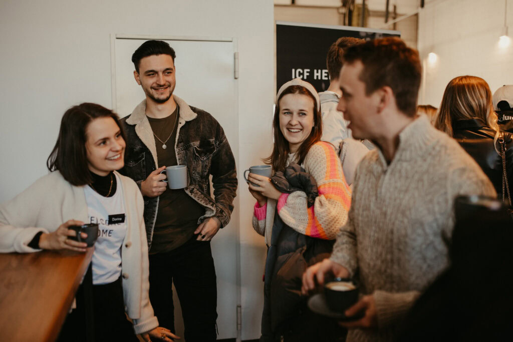 Fünf Menschen stehen in einer Bar, lachen und trinken Kaffee.