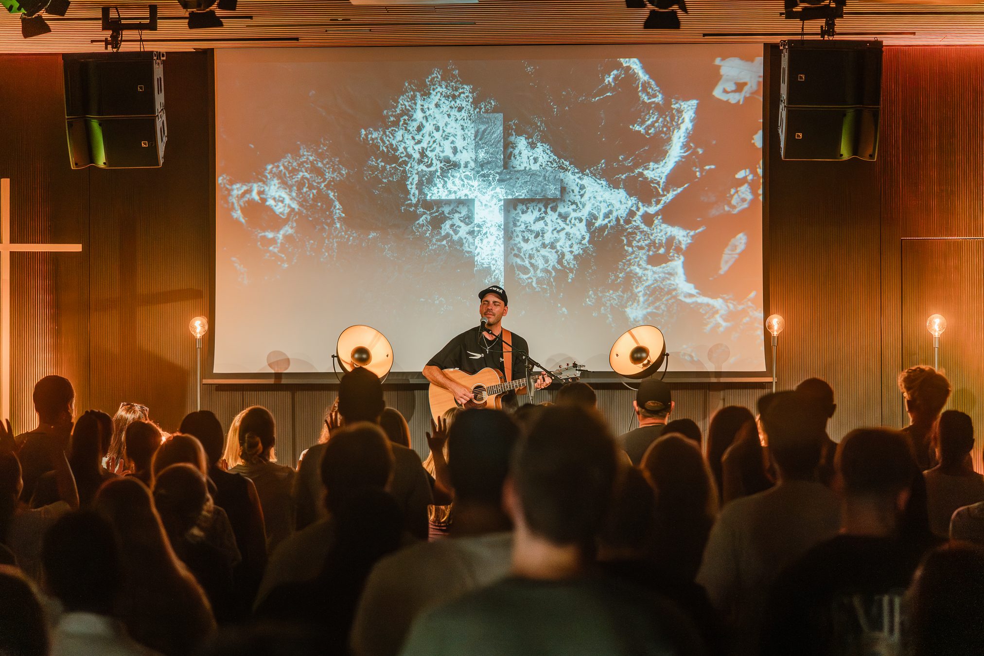 Musiker spielt Gitarre vor Publikum mit digitaler Projektion im Hintergrund.