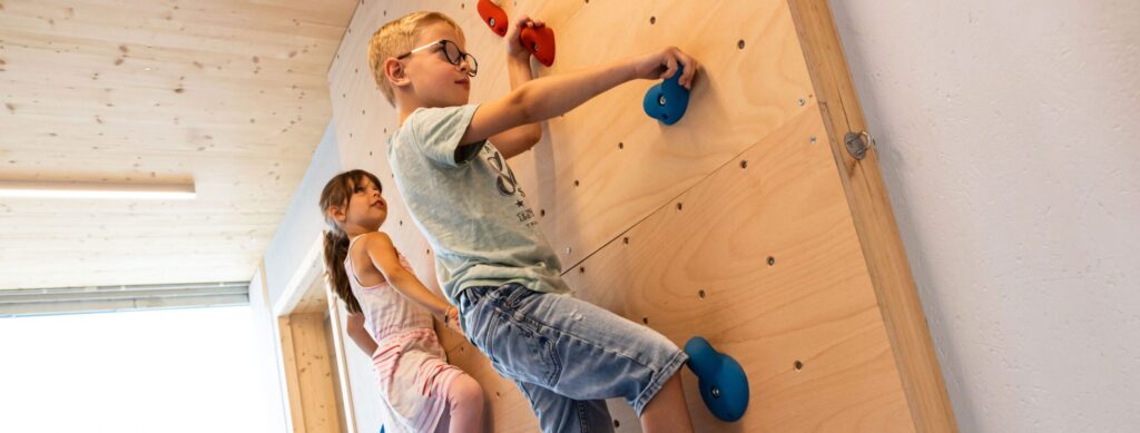 Zwei Kinder beim Klettern an einer Holz-Kletterwand.