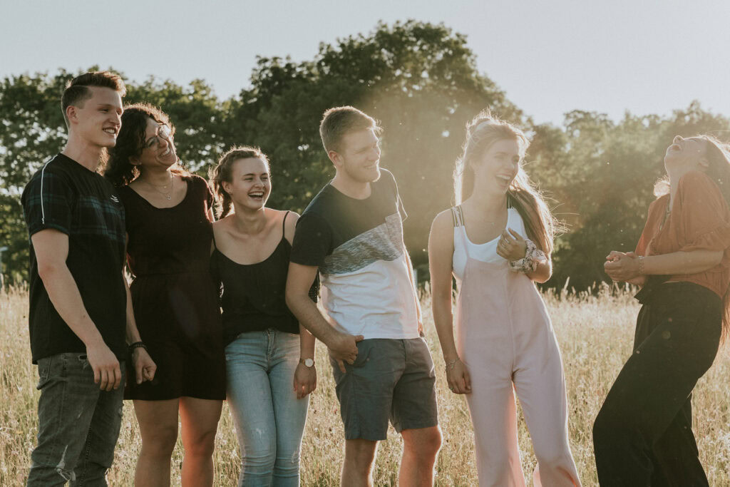Sechs junge Menschen stehen im Freien, lachen und sprechen miteinander.