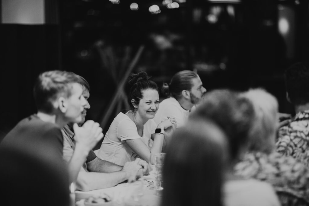 Mehrere Personen sitzen an einem Tisch, einige lachen und unterhalten sich.