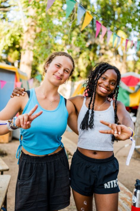 Zwei lachende Frauen beim Outdoor-Fest in Karlsruhe, feiern gemeinsam unter bunten Fahnen, umgeben von Natur und festlicher Atmosphäre.
