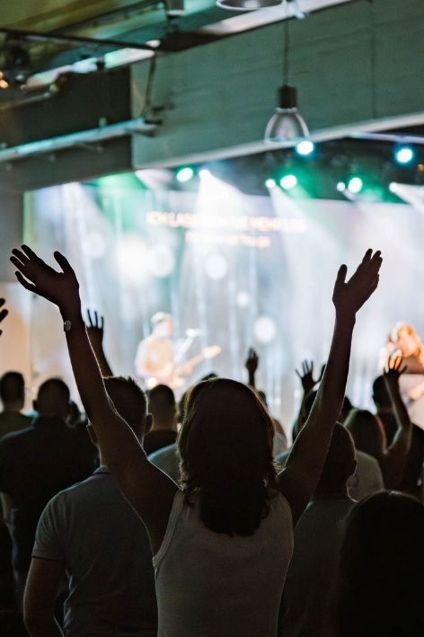 Menschen beim Gottesdienst in Karlsruhe mit erhobenen Händen, lebendige Atmosphäre, moderne Kirche, Gemeinschaft, Worship, christliche Veranstaltung.