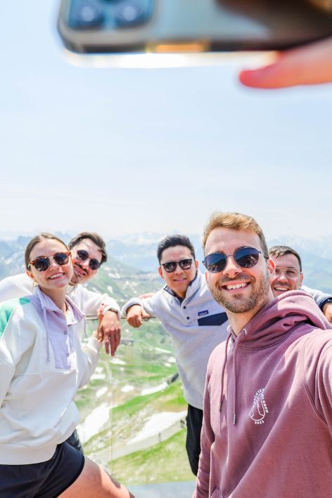 Gruppe junger Menschen macht ein Selfie mit Blick auf Karlsruhe im Hintergrund, sonniger Tag, fröhliche Stimmung, moderne Stadtlandschaft.