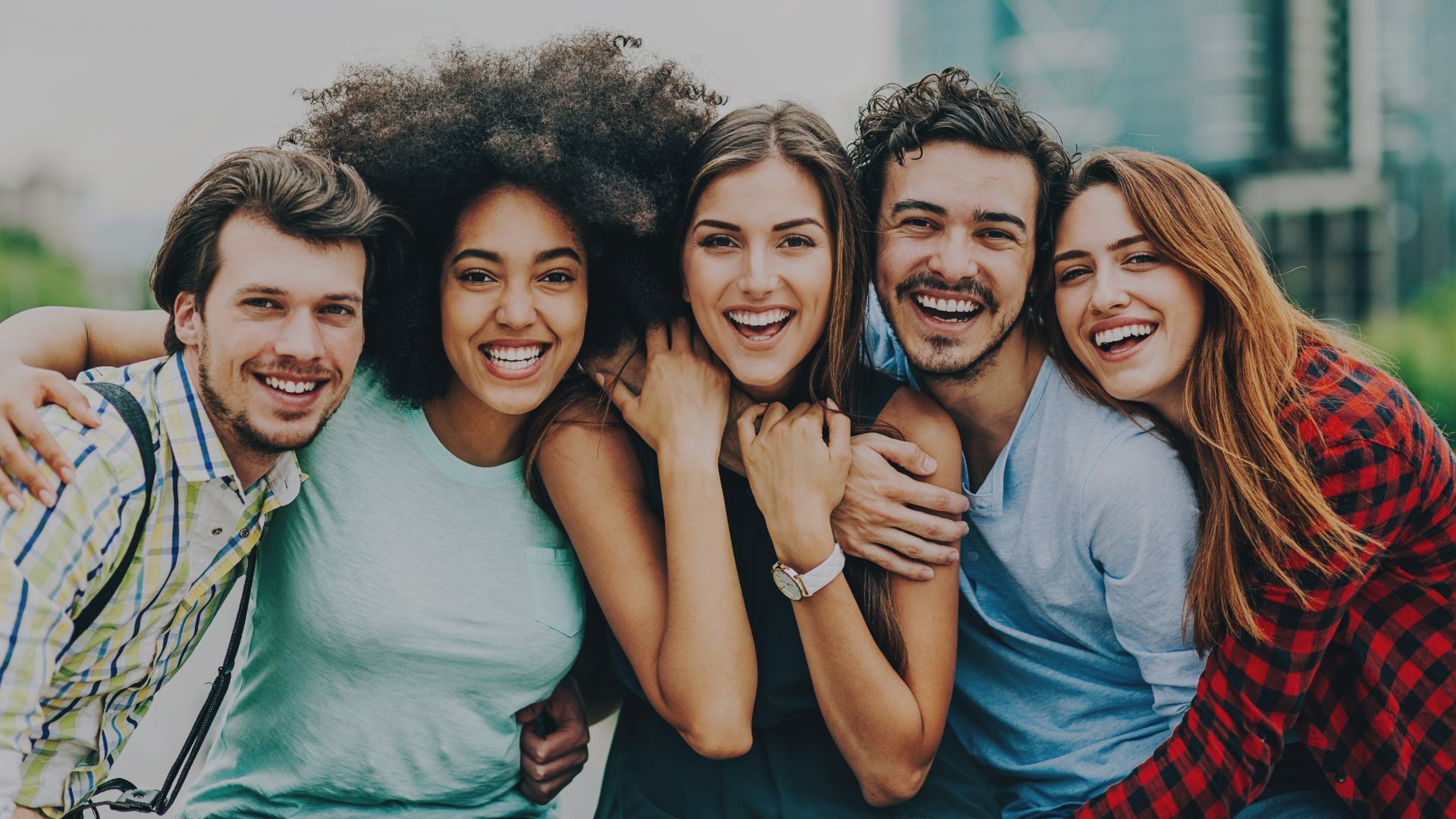 Fünf junge Menschen stehen eng beieinander, lachen und posieren im Freien.