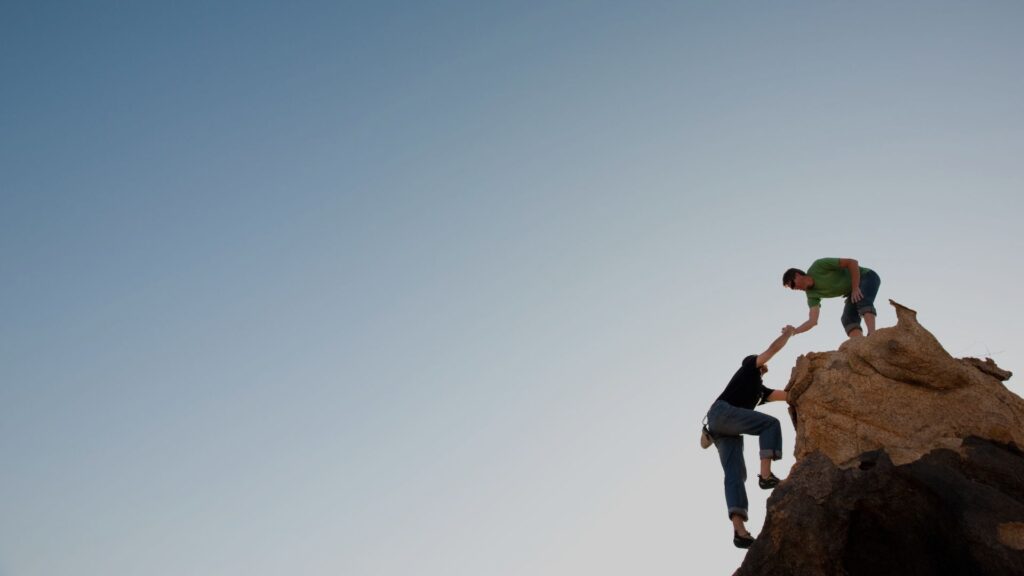Zwei Kletterer helfen sich gegenseitig beim Aufstieg auf einen Felsen.
