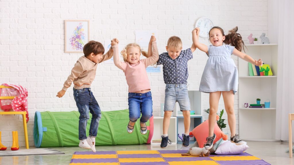 Fünf Kinder springen gemeinsam auf einem bunten Teppich.