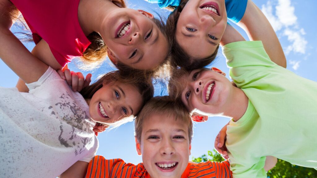 Gruppe von fünf lachenden Kindern im Kreis, Blick nach unten, blauer Himmel.