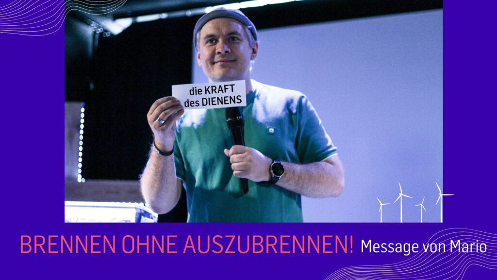 Mann hält ein Schild mit der Aufschrift "die KRAFT des DIENENS" vor einem Mikrofon.