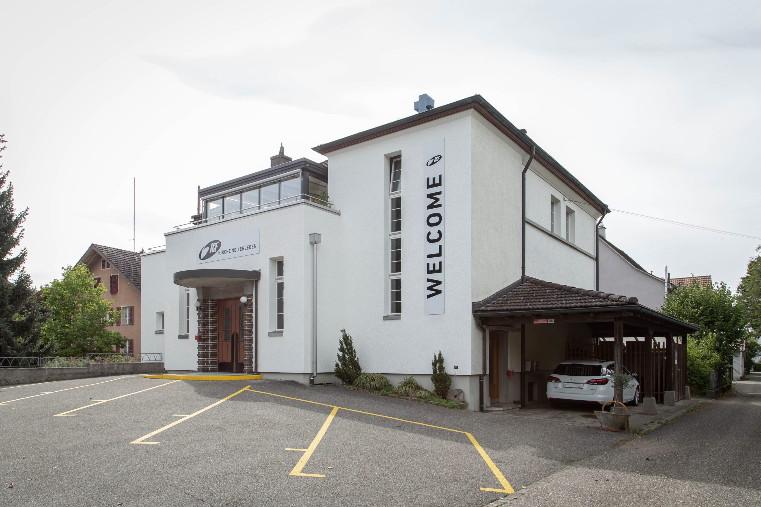 Weißes Gebäude mit "WELCOME" Schriftzug und Parkplätzen.