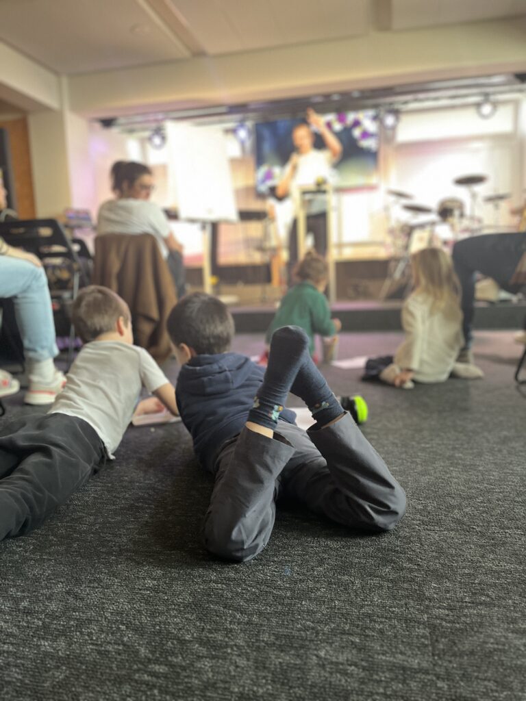 Enfants assis sur le sol regardant un adulte jouer de la guitare.