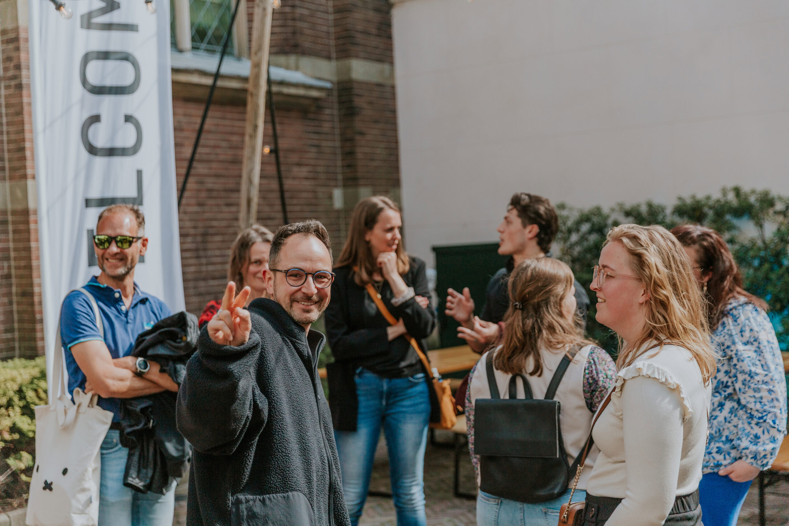 Groep mensen die buiten praten en lachen, met één persoon die een peace-teken maakt.