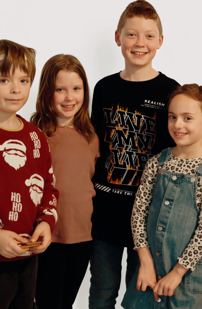 Vier lachende Kinder stehen nebeneinander vor weißem Hintergrund.