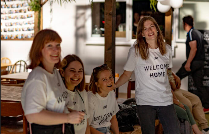 Gruppe von vier lachenden Frauen bei einer Veranstaltung im Innenbereich.
