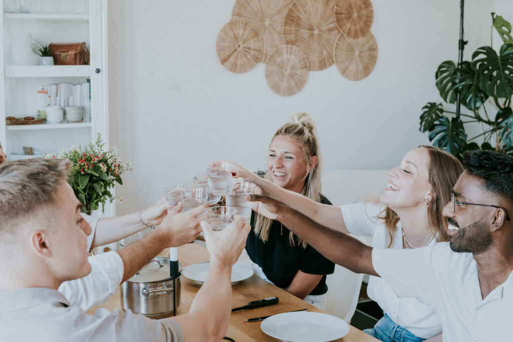 Fröhliche Menschen beim gemeinsamen Wohnen und Essen, Familie oder Freunde, gesellschaftliches Beisammensein, gemütliches Zuhause, gemeinschaftliches Dinner, freundschaftliche Atmosphäre, inklusive Gemeinschaftsleben.