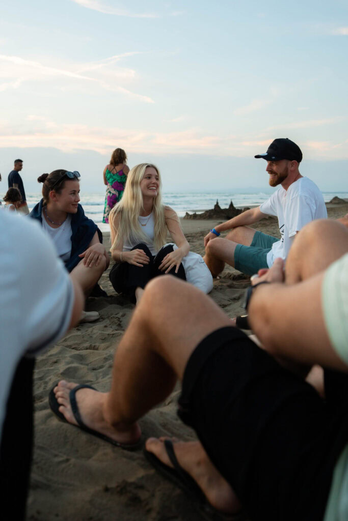 Menschen sitzen im Kreis am Strand bei Sonnenuntergang.