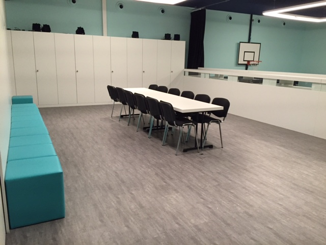 Raum mit Tisch, acht Stühlen, Couch, weißen Schränken und Basketballkorb an der Wand.
